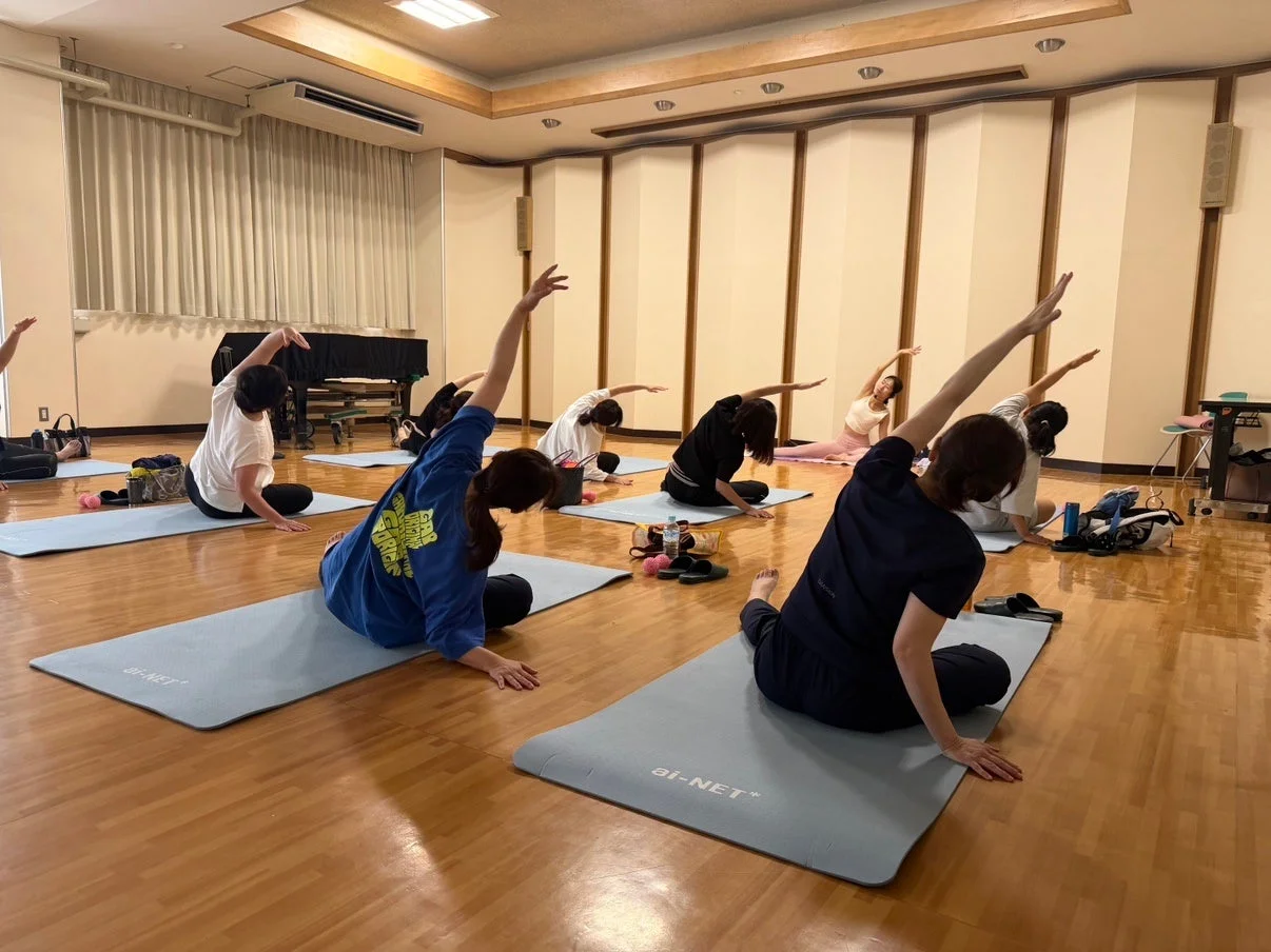 室内で複数の人々がヨガマットの上でストレッチやヨガを行っている様子