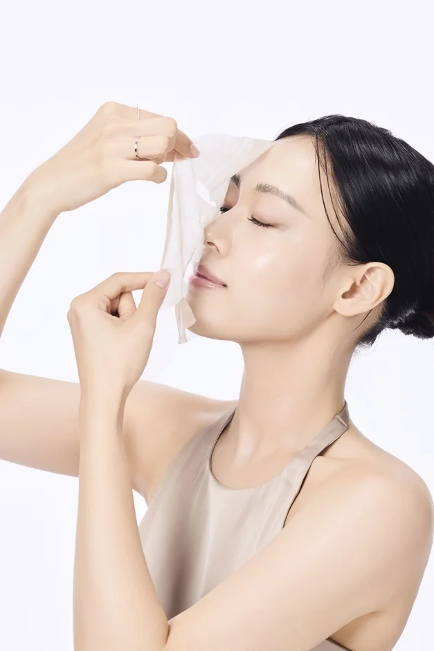 目を閉じた女性が顔からシートマスクをゆっくりと剥がしている画像