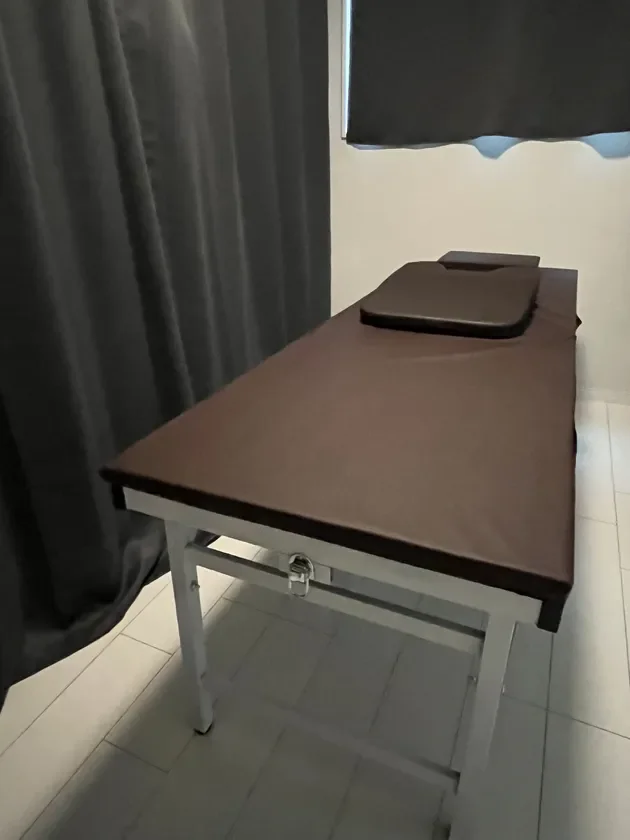 暗い色のカーテンと白い床の部屋に置かれた、茶色の施術台