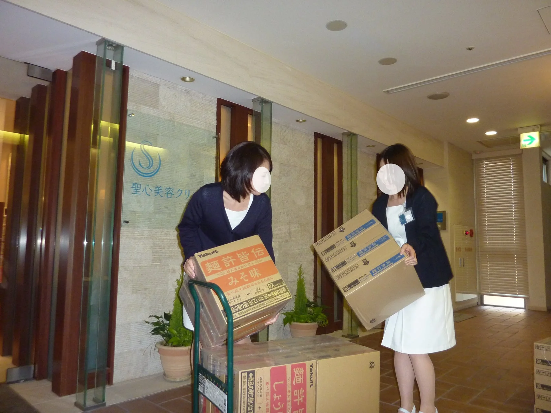 ヤクルトの麺許皆伝の段ボール箱を運ぶ女性たち