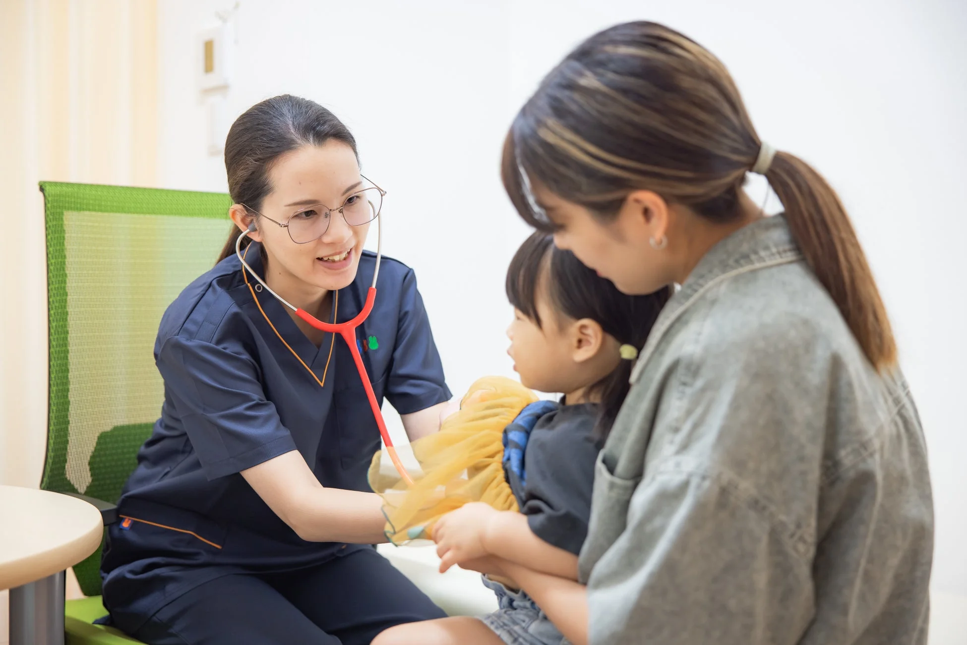 女性医師が母親に抱かれた小さな女の子を診察している様子