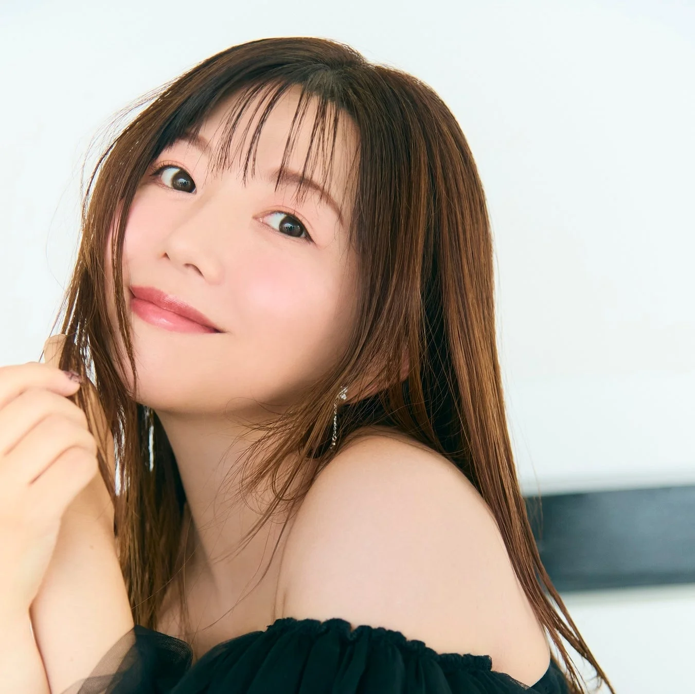 長い茶髪と前髪の若い女性が、黒いオフショルダーの服を着て優しく微笑んでいます