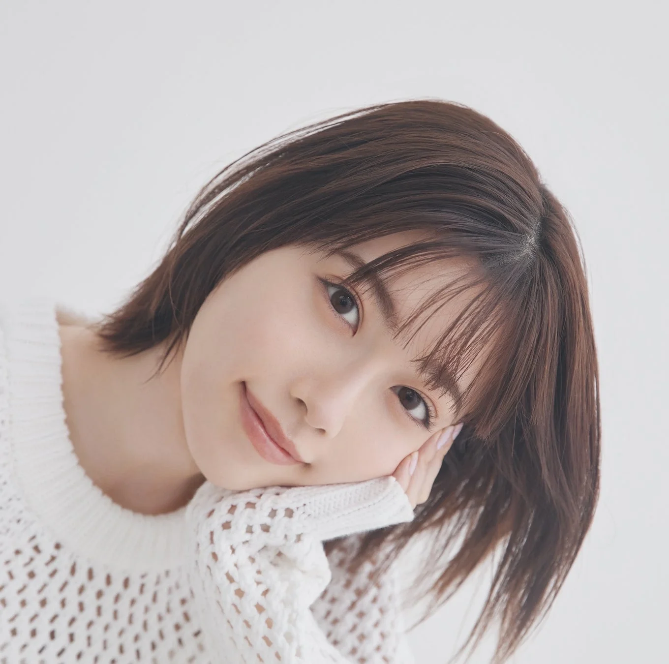 白いニットを着たショートヘアの女性が、顔に手を添えて優しい笑顔を見せているポートレート写真